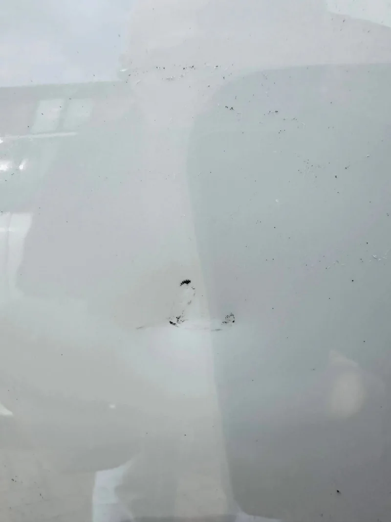 Close-up of the dent in a white Porsche Cayenne door before repair, with the damaged area circled in red